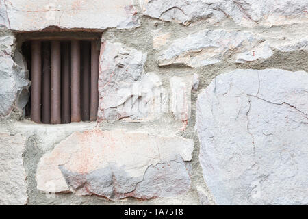 Alte Steinmauer mit kleinen eisernen Gefängniszelle Fenster gesperrt. Stockfoto