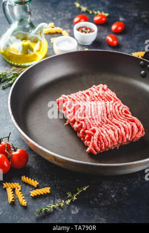 Frisches rohes Hackfleisch in einer Pfanne und Zutaten auf dunklem Hintergrund. Stockfoto