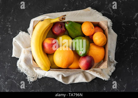 Große Holzkiste mit reifem Obst, Banane, Apfel, Orange, Mandarine, Avocado, vegetarische Essen Stockfoto