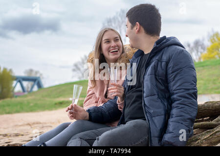 Ein junges Ehepaar sitzt am Strand halten Gläser in den Händen und Lachen Stockfoto