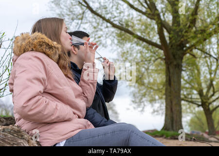 Junges Paar ist am Strand zu sitzen, die Gläser in der Hand und Trinken Stockfoto