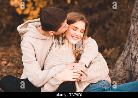 Glücklich Liebe Paar og Teenager sitzen unter Baum im Freien. Junge Mädchen küssen. Teenagerhood. Stockfoto