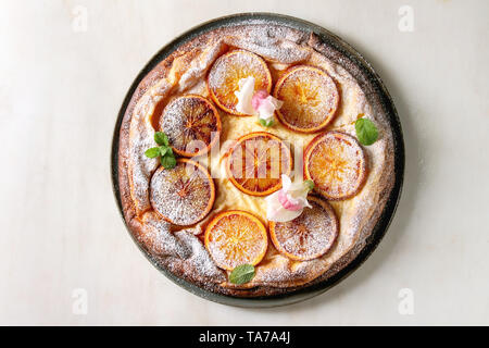 Hausgemachter Käsekuchen mit sizilianischer Blutorangen, dekoriert von essbaren Blüten, Minze und Zucker Pulver in der Platte mit geschnittenen Orangen oben o serviert. Stockfoto