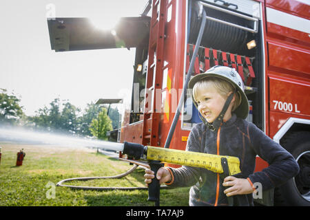 Kleiner Junge, sich wie ein Feuerwehrmann Holding firehose Düse und Spritzwasser. Stockfoto