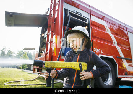 Kleiner Junge, sich wie ein Feuerwehrmann Holding firehose Düse und Spritzwasser. Stockfoto