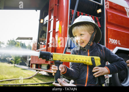 Kleiner Junge, sich wie ein Feuerwehrmann Holding firehose Düse und Spritzwasser. Stockfoto