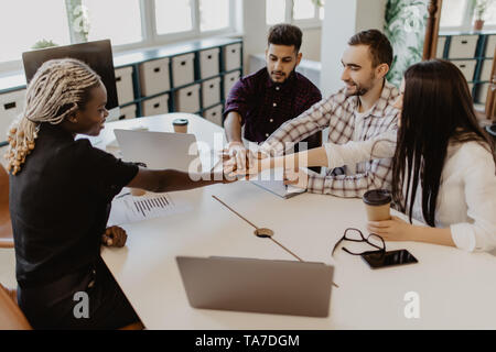 Gruppe von Happy business Menschen halten sich an den Händen zusammen, während sie rund um den Schreibtisch Stockfoto