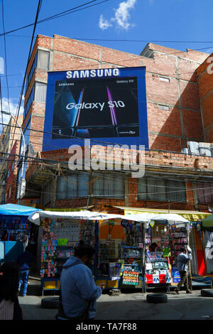 Mann mit Smartphone hinter Samsung Galaxy S10 Smartphone Werbung auf elektronische Anschlagtafel auf Backsteingebäude in Schmuggelware electronics Market Area, La Paz, Bolivien Stockfoto