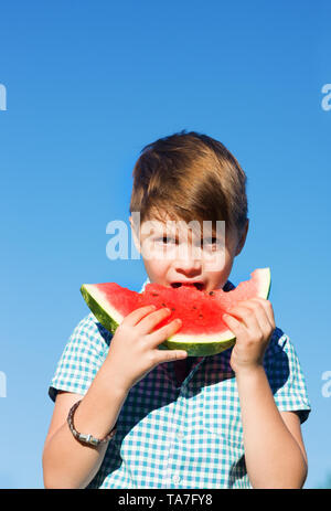 Funny Boy Eats Wassermelone im Freien gegen den blauen Himmel Stockfoto