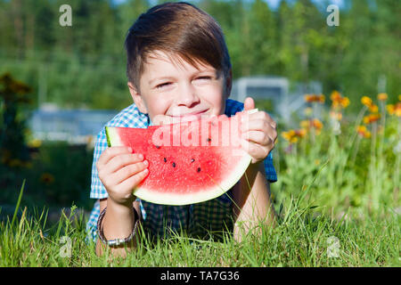 Funny Boy Eats Wassermelone im Freien im Sommer Park, gesundes Essen Stockfoto