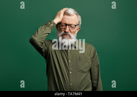 Attraktive alte Mann in Grün T-Shirt leiden unter Kopfschmerzen, intrakranieller Druck. nach oben Porträt schließen. Müdigkeit, gesundheitliches Problem, Migräne. Stockfoto