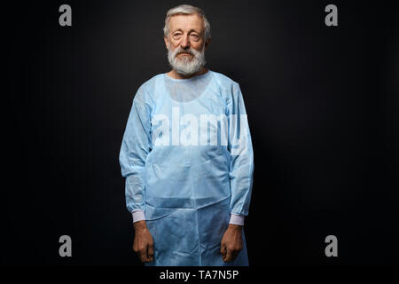 Gut aussehenden alten Chirurg nach Betrieb. Isolierte schwarze Hintergrund. Ruhige geisteskranken Mannes in die Kamera schaut Stockfoto