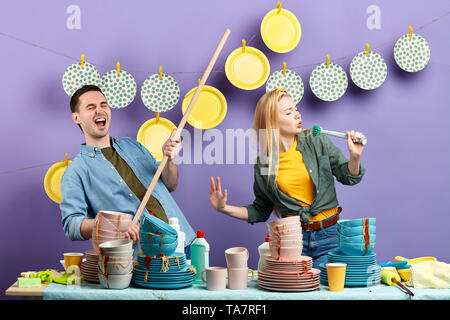 Junge emotionale Paar mit Pinsel und Besen tanzen und singen, während Sie eine Waschmaschine im Haus. Stockfoto