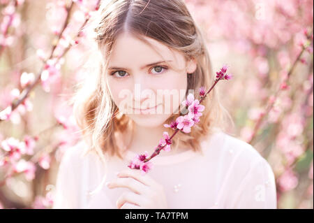 Lächelnde Mädchen mit Blumen in Peach Orchard. Mit Blick auf die Kamera. Frühling. Stockfoto