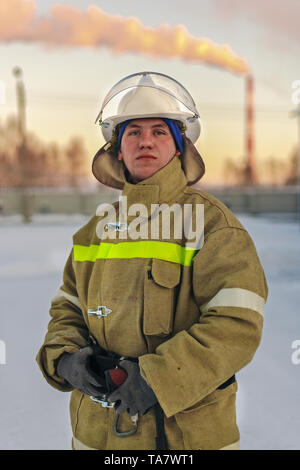 Portert Feuerwehrmann. Ein weißer Mann im Overall und Helm steht im Winter von drinnen nach draußen und schaut direkt in die Kamera. Stockfoto