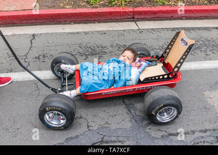 Ein Hispanic toddler legt in einem roten Radio Flyer custom kids Wagen als er State Strasse entlang an den Angehörigen Premier Car Show in Santa Barb gezogen wird. Stockfoto