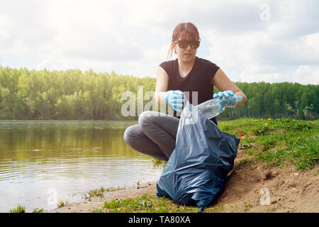 Foto von Mädchen in Gummi Handschuhe mit schmutzigen Kunststoff Flasche in der Hand am Ufer im Sommer Stockfoto