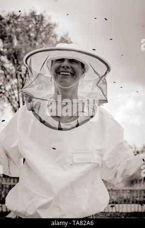 Ein lächelndes Imker Frau/apiarist Porträt trägt einen weißen Kittel mit Hut und Schleier, die während der Arbeit mit ihren Bienen - Imkerei/Bienenhaltung. B/W Stockfoto