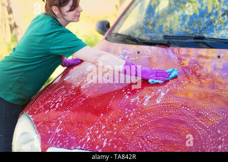 Frau in Gummi Handschuhe wäscht ein rotes Auto. Reinigungsmittel Stockfoto