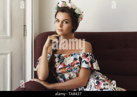 Porträt der jungen Frau im schönen Kleid sitzt auf dem alten Sofa Stockfoto