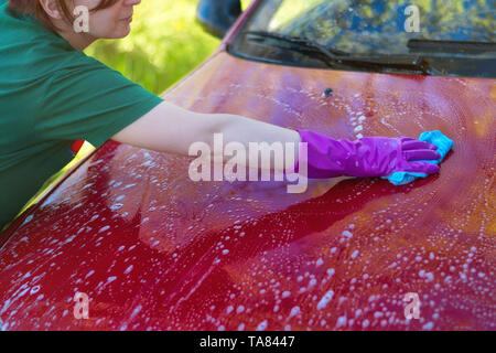 Frau in Gummi Handschuhe wäscht ein rotes Auto. Reinigungsmittel Stockfoto