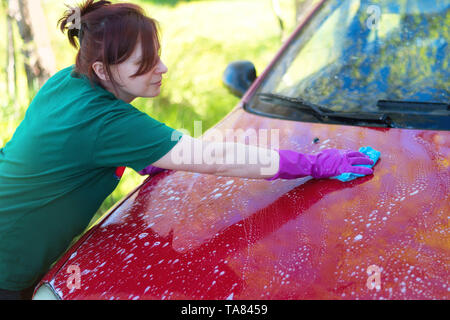 Frau in Gummi Handschuhe wäscht ein rotes Auto. Reinigungsmittel Stockfoto