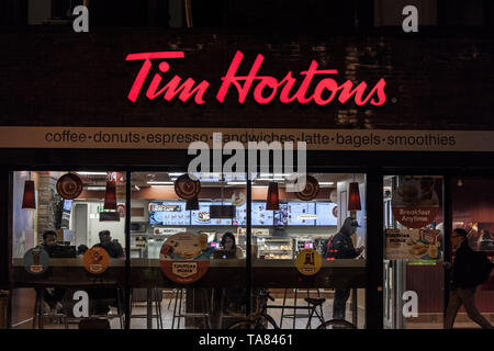 TORONTO, KANADA - 14. NOVEMBER 2018: Tim Hortons Logo vor einem ihrer Restaurants in Toronto, Ontario, in der Nacht, mit Fußgängern vorbei. Ti Stockfoto