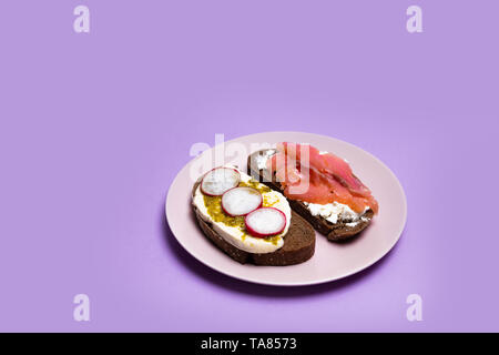 Frühstück mit verschiedenen Sandwiches mit verschiedenen Füllungen: mit Fisch, Käse und Gurke auf einem violetten Hintergrund. Stockfoto