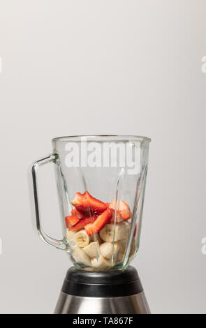 Süße Erdbeeren und Scheiben von reifen Bananen in Blender auf Grau Stockfoto