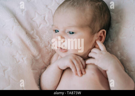 Cute adorable newborn baby Mädchen in einem Bett und in rosa Decke gewickelt. Neu geborene Kind, kleines Mädchen schauen in die Kamera überrascht. Familie, neue Leben, Stockfoto