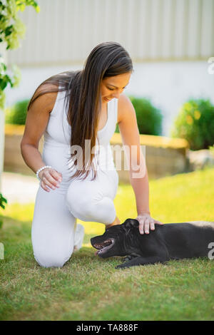 Lächelnd schwangere Frau mit einem großen Bauch streichelt ihr Hund im Garten Stockfoto