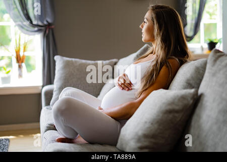 Lächelnd schwangere Frau sitzt im Sofa ihr Bauch berühren. Stockfoto