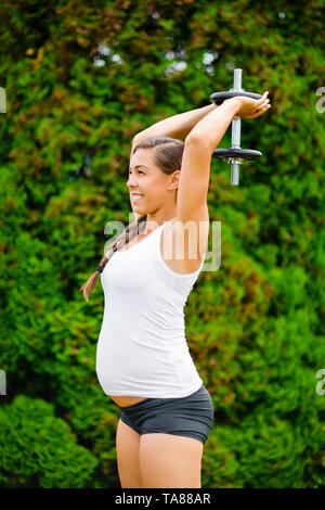Schwangere Frau Durchführung Trizeps Verlängerung Übung in Park Stockfoto