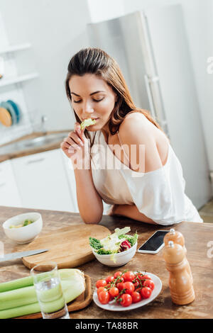 Nachdenkliches Mädchen am Tisch sitzen und essen Salat in der Küche Stockfoto