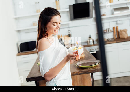 Lächelnde junge Frau mit Schüssel und essen frisches Obst in der Küche Stockfoto