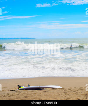 Surfboard auf sandigen Strand, Surfer reiten auf den Wellen im Hintergrund, Bali, Indonesien Stockfoto