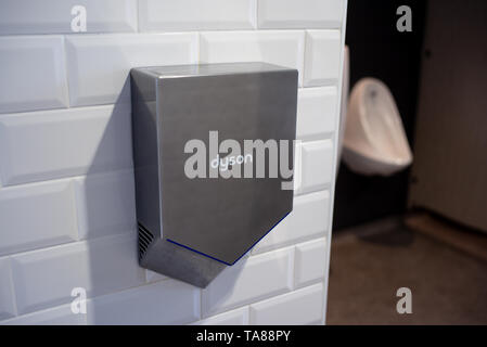 Eine abgewinkelte Dyson Händetrockner in einem öffentlichen WC mit Urinal im Hintergrund. Stockfoto