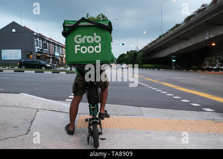 Ein Lebensmittel cycle Rider greifen auf den Straßen von Singapur der Lieferung von Nahrung an einer Kreuzung von einer viel befahrenen Straße als Regen Sturm bewegt sich in für ein dramatisches Bild warten. Stockfoto