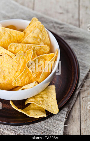 Mexikanische nachos Chips in weiße Schüssel auf braun Keramikplatte closeup auf Leinen Tischdecke. Rustikal Hintergrund. Stockfoto