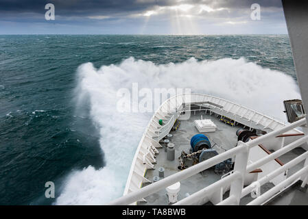 Vorderseite eines Schiffes, das durch schwere Wellen vor der Küste von Spitzbergen mit Sonnenstrahlen (Gottesstrahlen oder Crepuskulösen Strahlen) in der Ferne stürzt. Stockfoto