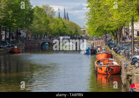 Amsterdam Canal Boote und eine Kanalbrücke - Frühling Tag in Amsterdam mit der typischen Amsterdamer Architektur und Kirchtürmen Stockfoto