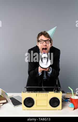Wütend Geschäftsmann am Arbeitsplatz in der Partei in der Nähe von gap Vintage tape recorder im Megaphon schreiend auf grauem Hintergrund Stockfoto