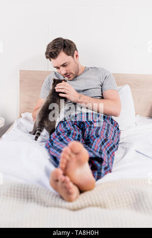 Selektiver Fokus der gutaussehenden Mann in Plaid Shirt im Bett lag, mit niedlicher Waschbär. Stockfoto