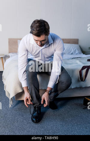 Schöner Mann, schwarze Schuhe, sitzend auf Betten zu Hause Stockfoto