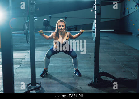 Gymnast Mädchen tun Hocke barbell. Vorderansicht der attraktive junge Frau Stockfoto