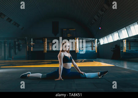 Stretching gymnast Mädchen tun Vertical Split, Garn. Seitenansicht der attraktive junge Frau tun core Übung bei crossfit Fitnessraum Stockfoto