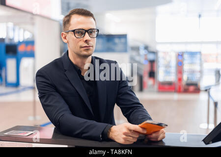 Business Reise. Hübscher junger Geschäftsmann in Anzug Holding seinen Pass und im Gespräch mit Frau am Check-in-Schalter im Flughafen Stockfoto