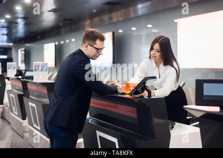 Business Reise. Hübscher junger Geschäftsmann in Anzug Holding seinen Pass und im Gespräch mit Frau am Check-in-Schalter im Flughafen Stockfoto