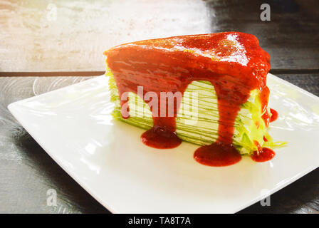 Crape Kuchen/grüner Tee crape Kuchen mit Erdbeersauce auf weiße Platte rustikal Holz Hintergrund Stockfoto