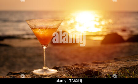 Cocktail Glas mit Meerblick und Blick auf den Strand im Hintergrund, während Sie am Sonnenuntergang Stockfoto